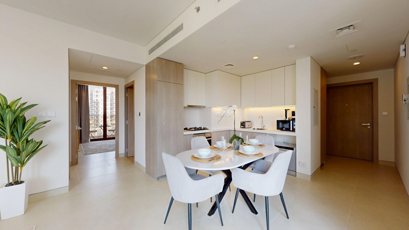 A modern kitchen with white cabinetry, a dining area with a round table and chairs, and a potted plant.
