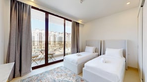 Ein Hotelzimmer mit zwei Betten, einem großen Fenster mit Vorhängen, Blick auf Gebäude und einem kleinen Tisch mit Stuhl.