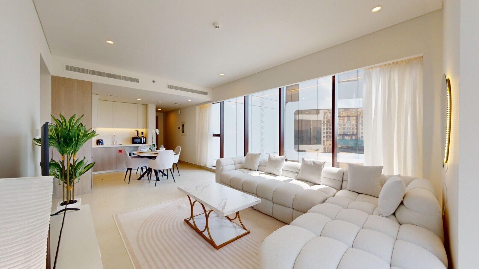 A modern living room with a large sectional sofa, a dining area with a table and chairs, and a kitchen in the background.