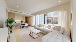 Una sala moderna con un amplio sofá modular, un comedor con mesa y sillas, y una cocina al fondo.