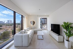 Ein modernes Wohnzimmer mit einem großen Ecksofa, einem Flachbildfernseher und Blick auf die Stadt.