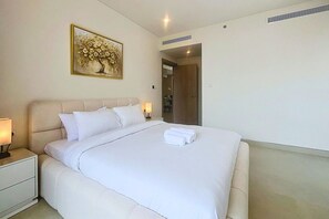 A hotel room with a bed, bedside tables, a lamp, a painting on the wall, and a door leading to a bathroom. - Minimalist 2 Bedroom l near Cricket Stadium (Dubai Sports City)