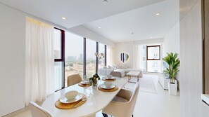 Ein modernes Hotelzimmer mit Essbereich, einer Sofagruppe und großen Fenstern mit Blick auf die Stadt.