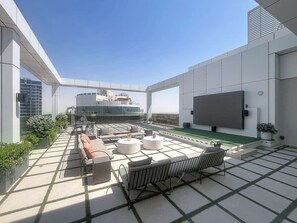 A rooftop terrace with outdoor seating, a flat-screen TV, and a view of the cityscape. - Minimalist 2 Bedroom l near Cricket Stadium (Dubai Sports City)