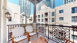 A balcony with two wooden chairs and a table, a decorative metal railing, and a view of surrounding buildings. - Central 1 Bed l Minutes Walk to Dubai Mall (Downtown)