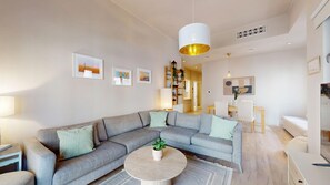 Ein modernes Wohnzimmer mit einem grauen Ecksofa, einem runden Couchtisch und einer hängenden Pendelleuchte.