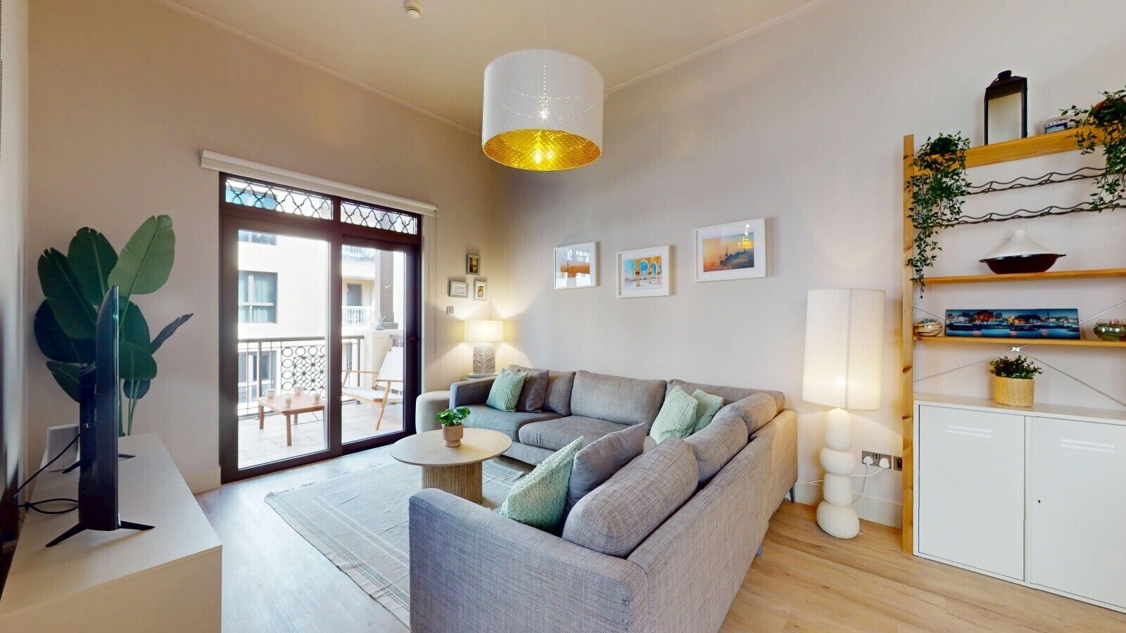 Een moderne woonkamer met een grijze bank, een ronde salontafel en een grote plant.