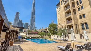 Ein Schwimmbecken mit Liegestühlen, Blick auf den Burj Khalifa und ein Gebäude mit Balkonen.