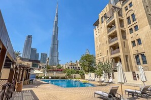 A swimming pool with lounge chairs, a view of the Burj Khalifa, and a building with balconies. - Central 1 Bed l Minutes Walk to Dubai Mall (Downtown)