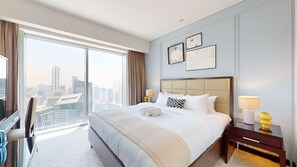 Ein Hotelzimmer mit einem großen Bett, einem Schreibtisch, einem Stuhl, einer Lampe und Blick auf die Stadt.