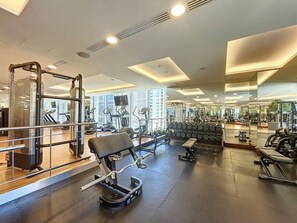 A gym with various exercise equipment, mirrors, and a view of buildings outside. - Overlooking 1 Bed l Skyline Views l Mall Access (Dubai Marina)