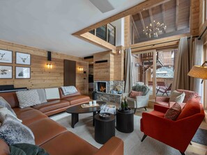A modern living room with a fireplace, leather sofas, and a red armchair. - Luxury chalet near slopes - 12 guests (Méribel)