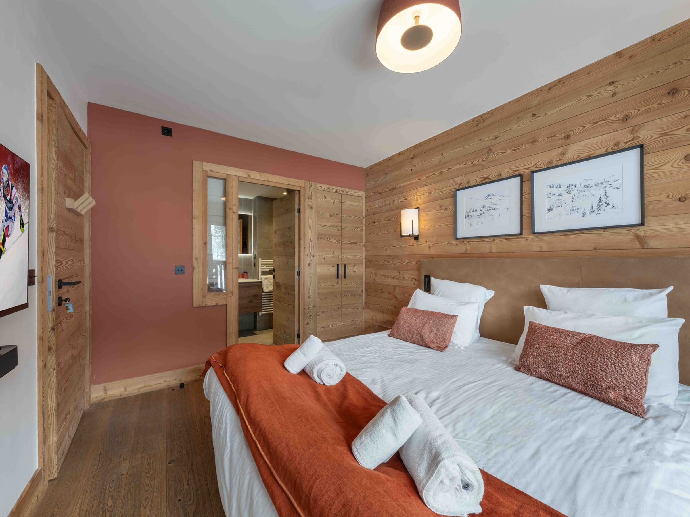 Een hotelkamer met een houten wandpaneel, een bed met witte lakens, twee kussens, een rode plaid en een ingelijst schilderij boven het bed.