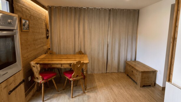 Quarto com uma mesa de madeira, duas cadeiras, um banco, micro-ondas e cortina.