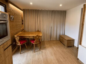 A room with a wooden table, two chairs, a bench, a microwave, and a curtain. - Central apartment, pets allowed - 5 guests (Châtel)