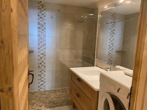 A modern bathroom with a glass-enclosed shower, a built-in washing machine, and a wooden vanity. - Central apartment, pets allowed - 5 guests (Châtel)