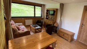 Um quarto aconchegante com uma mesa de madeira, um sofá, uma televisão e um armário.