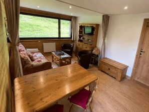 Ein gemütliches Zimmer mit einem Holztisch, einer Couch, einem Fernseher und einem Schrank.