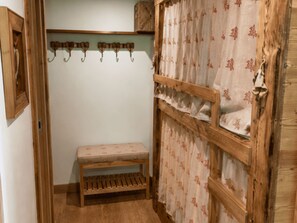 Ein Zimmer mit einer hölzernen Sitzbank, einem an der Wand befestigten Kleiderhaken und einem Vorhang mit einem Blumenmuster.