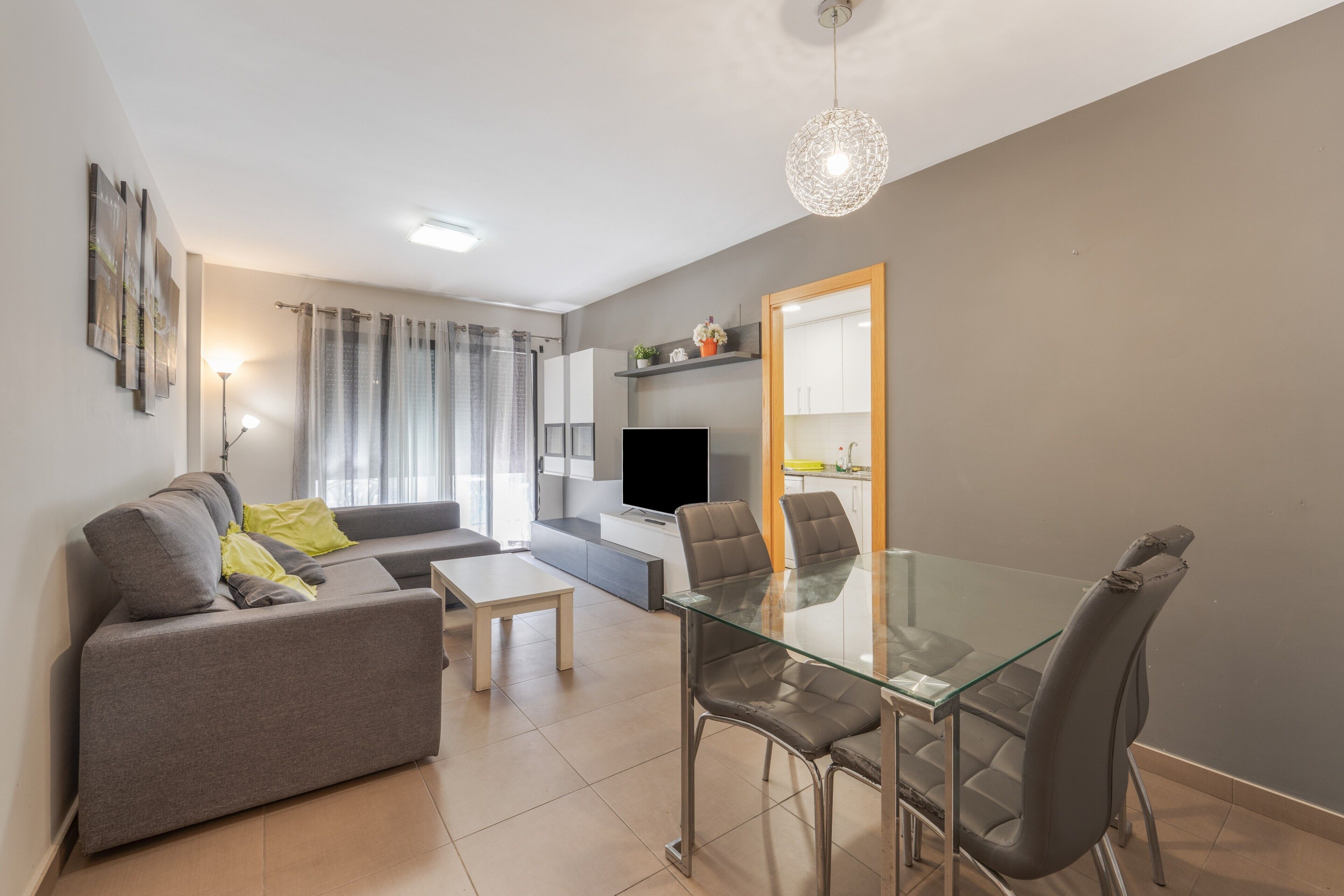 A modern living room with a sofa, a glass dining table, and a TV.