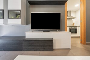A modern living room with a flat-screen TV on a white entertainment unit, a dark wood cabinet, and a kitchen in the background. - Apartment 'Edimar' with Balcony and Air Conditioning (Benidorm)