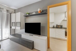 A modern living room with a flat-screen TV, a dark wood bench, and a kitchen area visible through an open door. - Apartment 'Edimar' with Balcony and Air Conditioning (Benidorm)