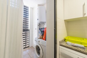 A compact laundry area with a washing machine, a drying rack, and a small countertop with a yellow basket. - Apartment 'Edimar' with Balcony and Air Conditioning (Benidorm)