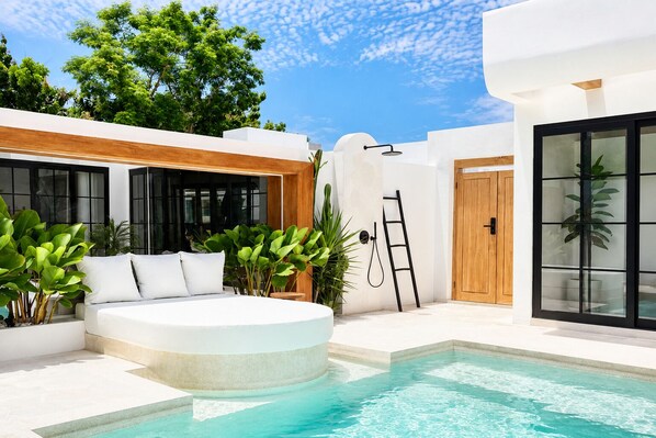 Uma área moderna de piscina ao ar livre, com um espaço de estar circular, uma escada e uma porta que dá para uma área coberta.