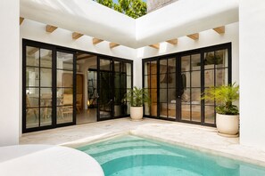 Uma área de piscina moderna com portas de vidro que dão para um alpendre, rodeada por vasos de plantas.