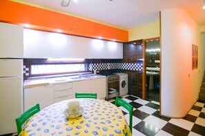 Eine kompakte Küche mit Essbereich, mit einem Schachbrettmuster-Boden, einem Tisch mit gemustertem Tischläufer und einem Kühlschrank.