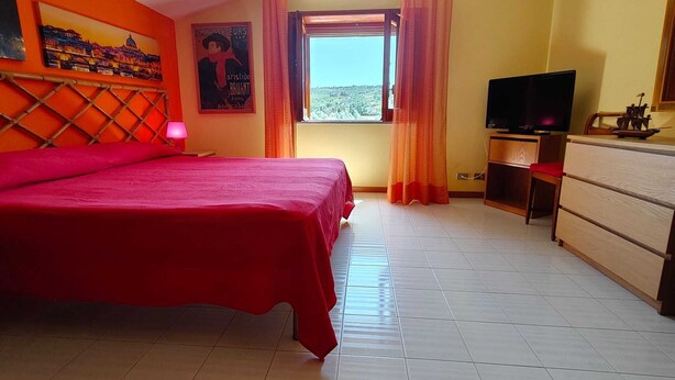 A bedroom with a large bed, a television, a dresser, and a window with curtains. - A retreat for relaxation and nature. (Ascea)