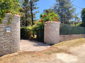 A gated entrance with a stone wall, a metal fence, and a paved path leading to a building. - A retreat for relaxation and nature. (Ascea)