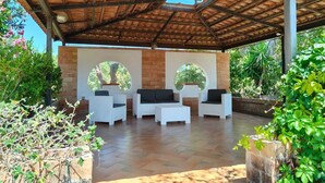 An outdoor patio with a brick wall, two round windows, and white wicker furniture. - A retreat for relaxation and nature. (Ascea)