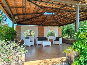 Eine Terrasse im Freien mit einer Ziegelwand, zwei Rundfenstern und weißen Korbmöbeln.