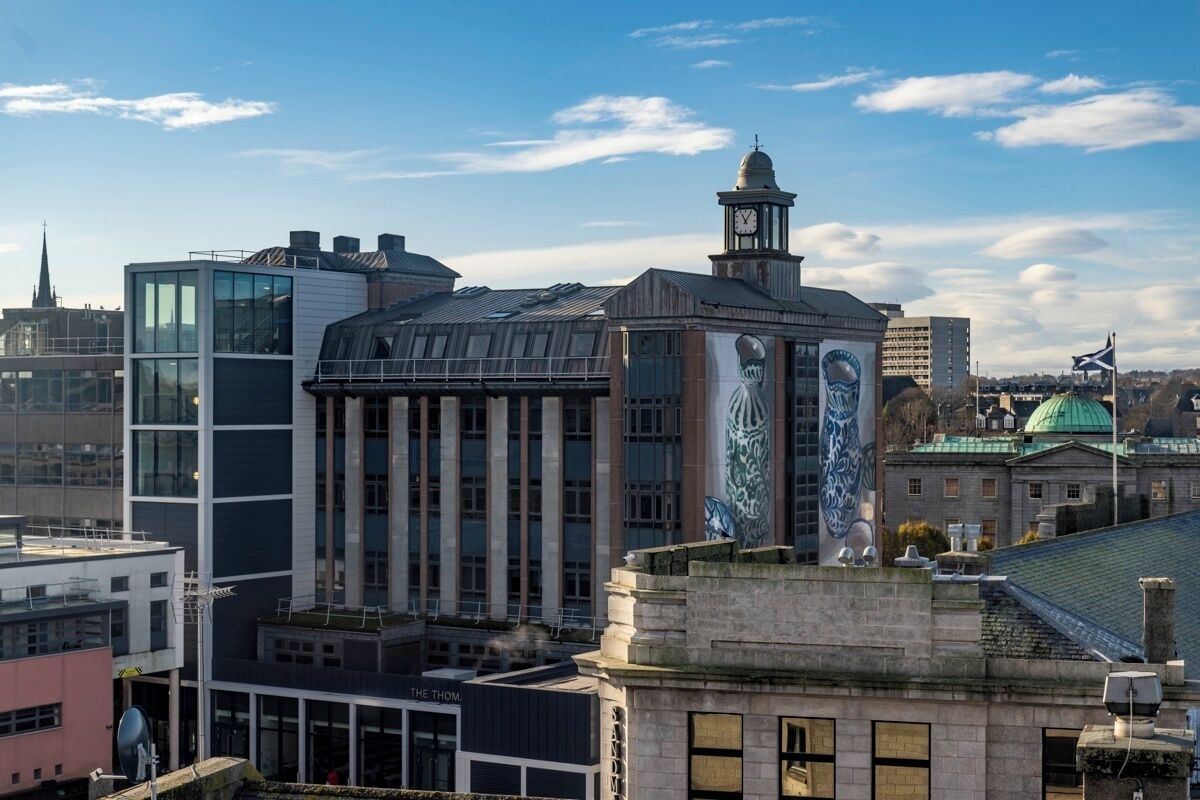 Un edificio histórico con una torre de reloj, ventanas grandes y un mural en la fachada.
