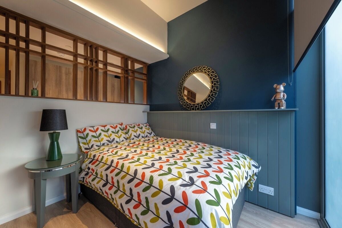 A bedroom with a bed, a bedside table with a lamp, a mirror, and a decorative item on the wall.