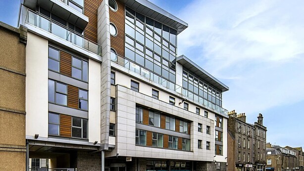 A modern multi-story building with a mix of glass and wood facade, featuring balconies and a ground-level entrance. - Student Only St Andrew Street (Aberdeen)