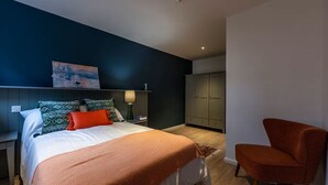 A bedroom with a bed, nightstand, lamp, wardrobe, and a chair. - Student Only St Andrew Street (Aberdeen)