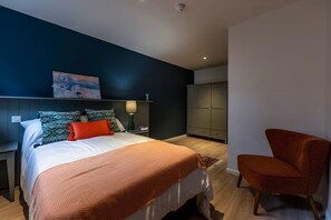 A bedroom with a bed, nightstand, lamp, wardrobe, and a chair. - Student Only St Andrew Street (Aberdeen)