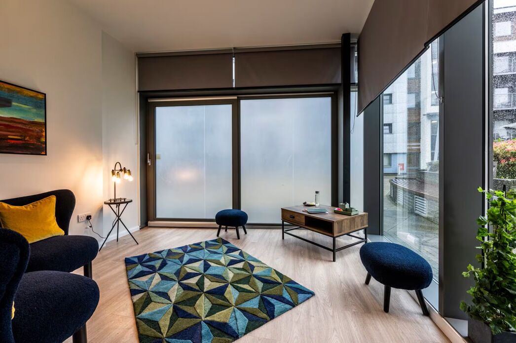 Ein modernes Wohnzimmer mit einer Couch, einem Couchtisch und einem Teppich. Ein großes Fenster bietet Blick ins Freie.