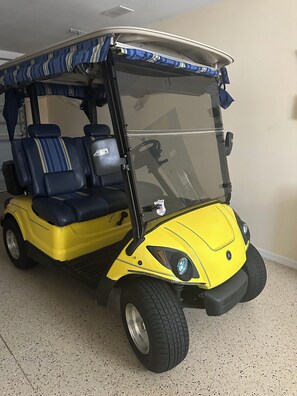 Ein gelber Golfwagen mit blauen Sitzen und einem Verdeck, geparkt in einem Innenbereich.