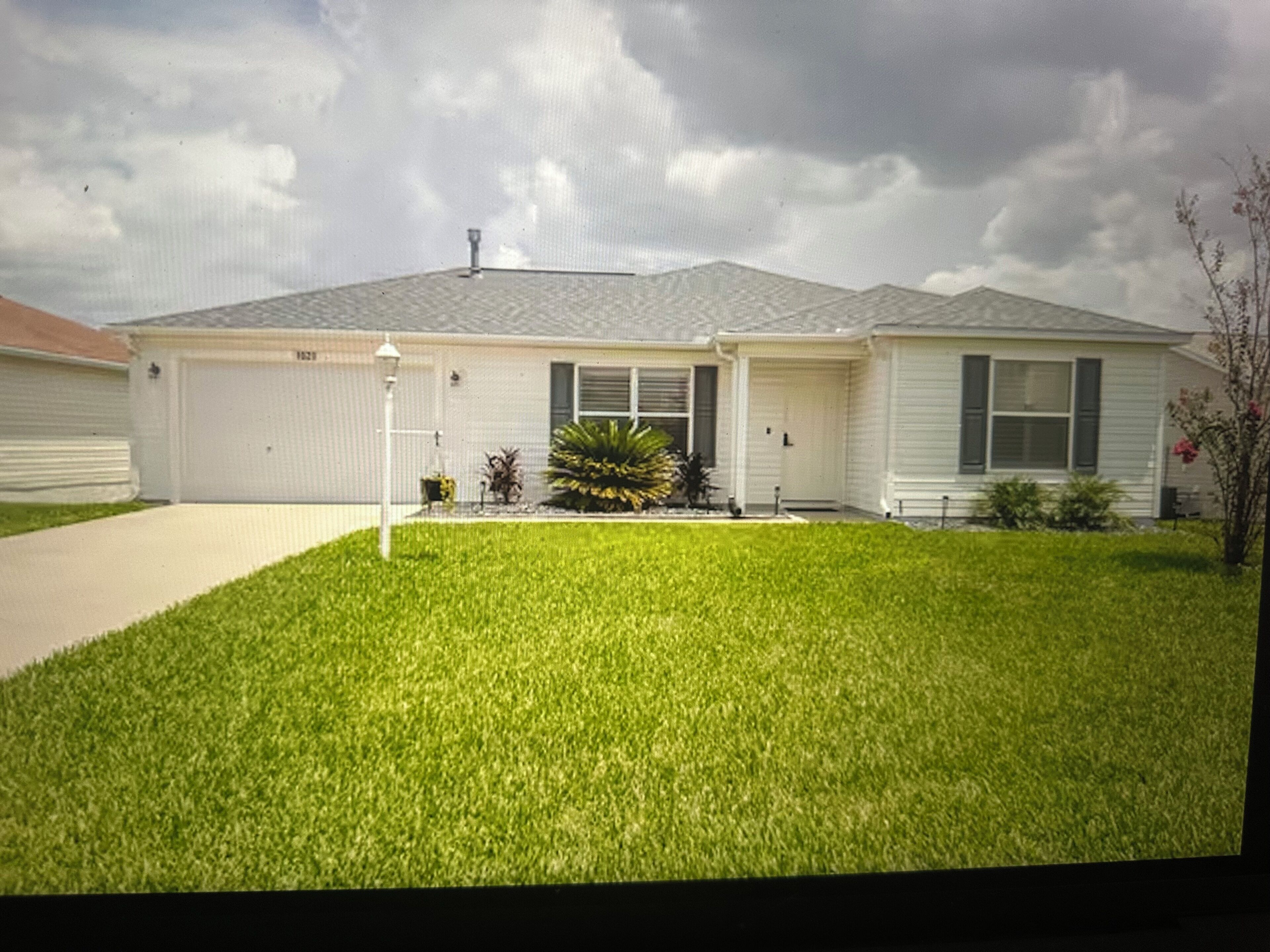 A single-story house with a front garage, a well-maintained lawn, and a small garden with a variety of plants.