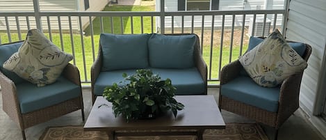 Une véranda couverte avec des meubles en osier, une table centrale agrémentée d’une plante et un tapis à motifs.