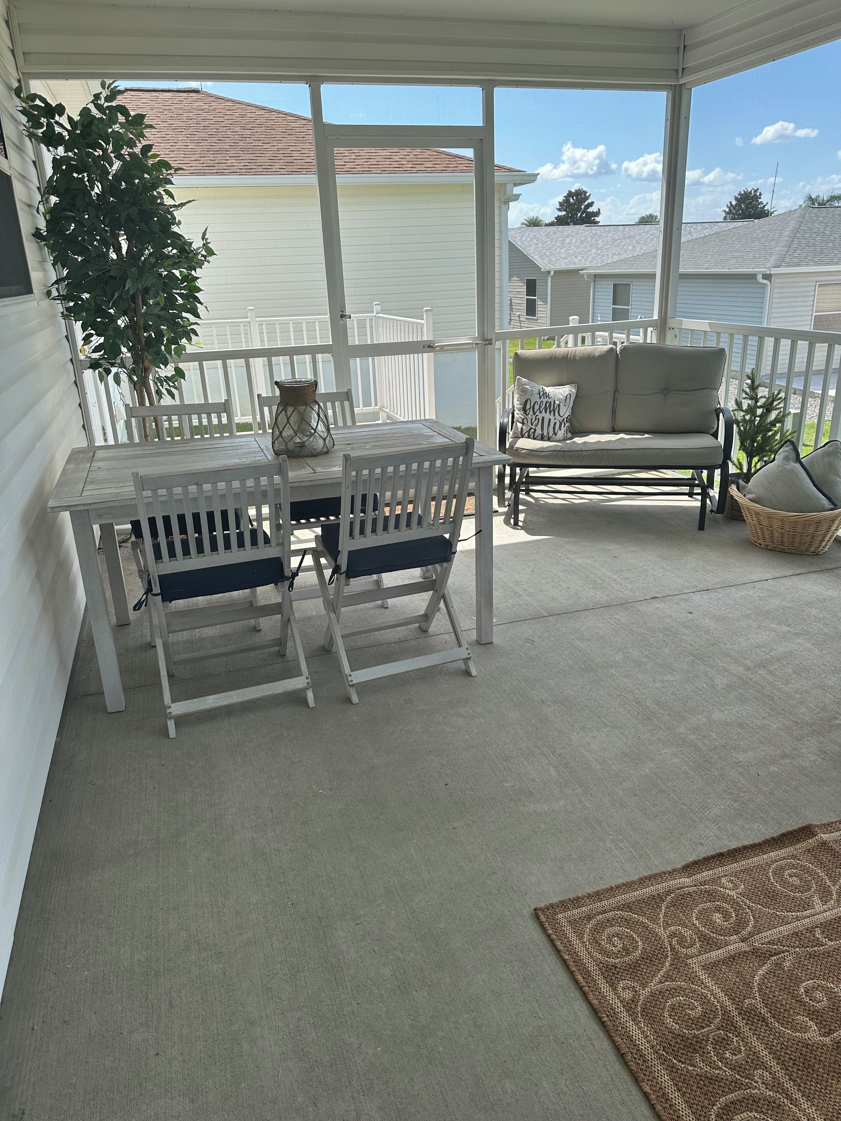A covered patio area with a table and chairs, a sofa, and a potted plant.