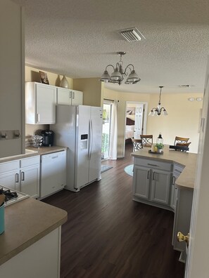 Eine moderne Küche mit weißen Schränken, einem Kühlschrank, einem Geschirrspüler und einem Essbereich mit Tisch und Stühlen.