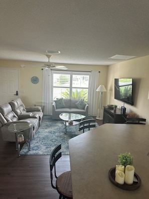 A living room with a sofa, coffee table, TV, and dining area. - 2-bedroom house in Lake Sumter The Villages includes Golf Cart (The Villages)