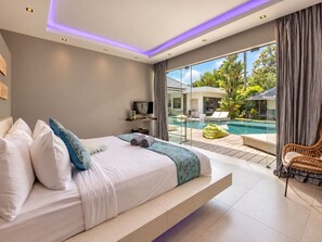 A modern bedroom with a bed, a television, and a view of a pool and outdoor area. - Spacious 4 BR villa Center Seminyak (Seminyak)