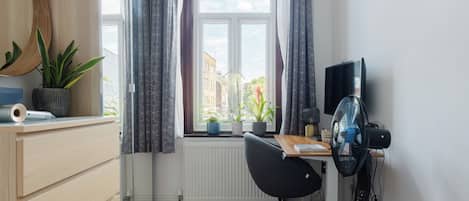 A modern office space with a desk, chair, and computer monitor. There is a window with curtains, a radiator, and a potted plant on the desk.