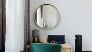 Ein Zimmer mit einem runden Spiegel, einem Schreibtisch mit Laptop, einem Mikrofon, einem Lautsprecher und einem Heizgerät.
