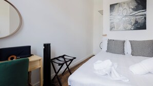 Ein Hotelzimmer mit Bett, Schreibtisch mit Computer, Stuhl, Heizlüfter und einem Bild an der Wand.